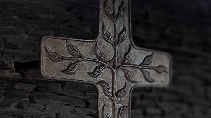 Ein Kreuz mit Baumrelief an einer Ziegelmauer.