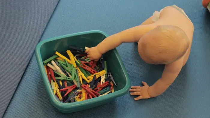 Ein Baby greift in einen Behälter mit bunten Spielsachen.