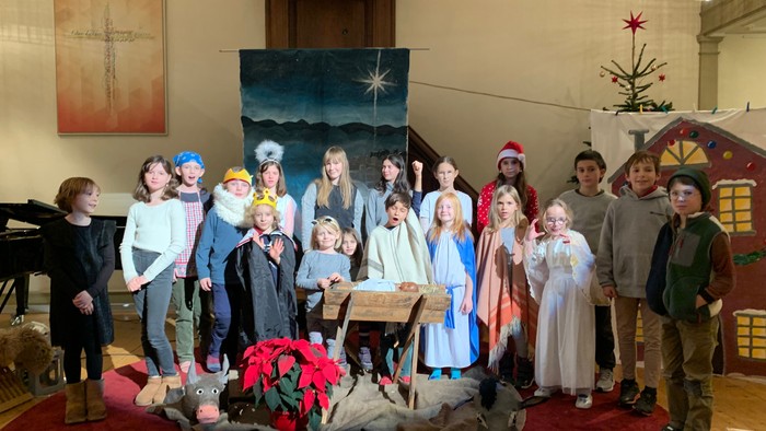 Kinder in Kostümen posieren vor einer Krippe