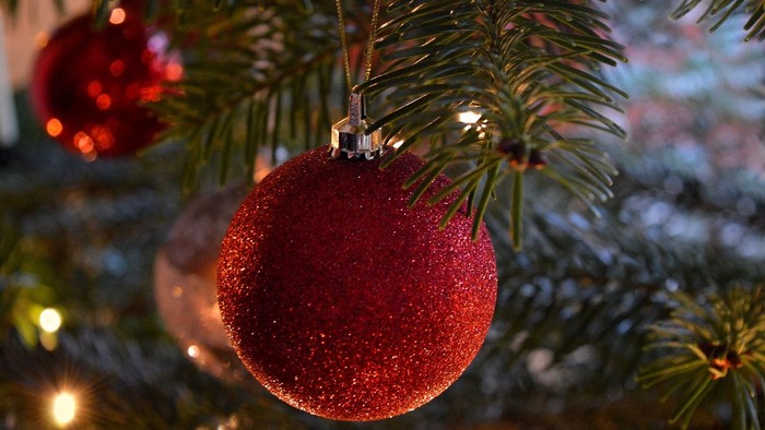 Ein glitzernder roter Christbaumschmuck hängt an einem Tannenzweig.