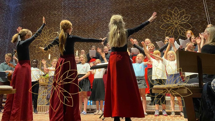 En gruppe kvinder i røde kapper danser på scenen foran en publikum.