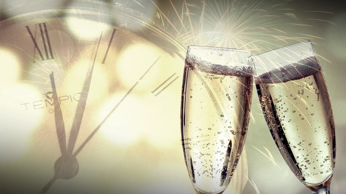 Zwei Champagnergläser bei Silvesterfeier mit Feuerwerk und Uhr.