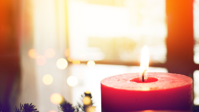Eine rote Kerze steht auf einem Tisch vor einem Fenster mit Weihnachtsbeleuchtung.