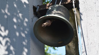 Eine Glocke ist an der weißen Wand befestigt.