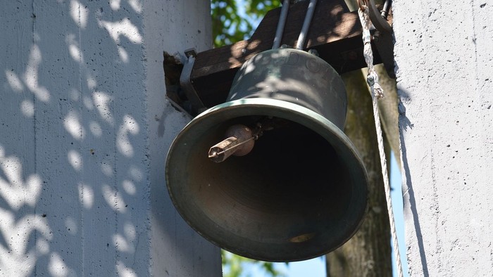 Eine Glocke ist an der weißen Wand befestigt.
