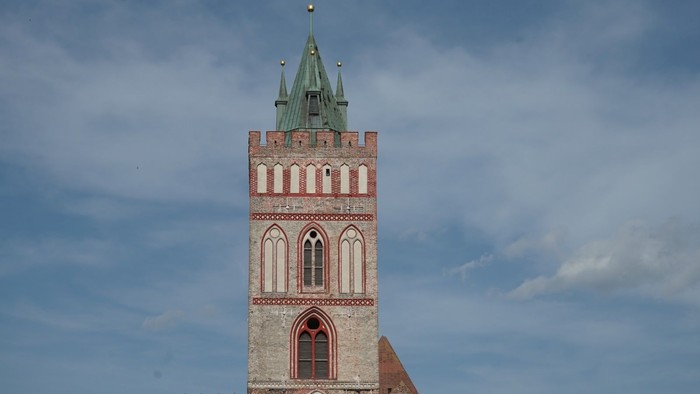 Turm einer historischen Backsteinkirche mit spitzem grünen Dach und gotischen Fenstern