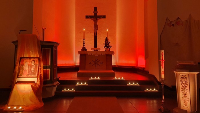 Eine Kirchenkulisse mit Kruzifix, Kerzen und Weihnachtsdekorationen.