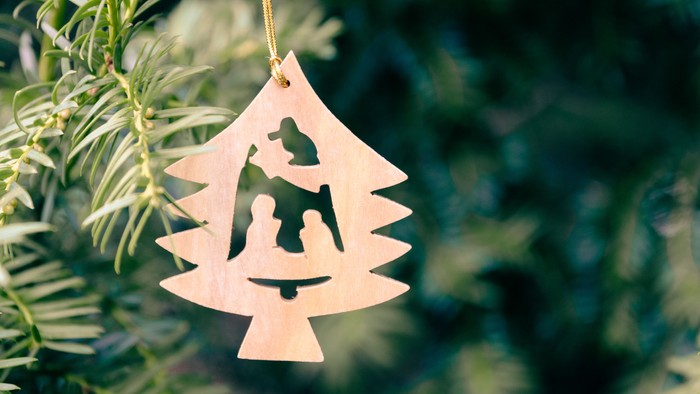 Ein hölzernes Weihnachtsbaum-Dekoration mit einer Silhouette der Heiligen Familie hängt an einem Tannenbaum.