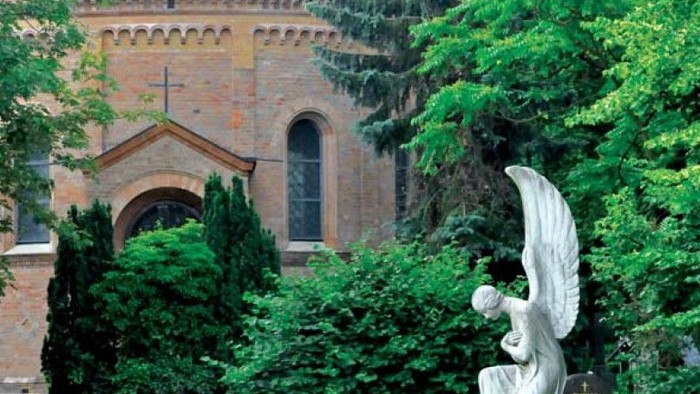 Ein Engel-Denkmal vor einer Kirche mit Kuppel und grünen Bäumen