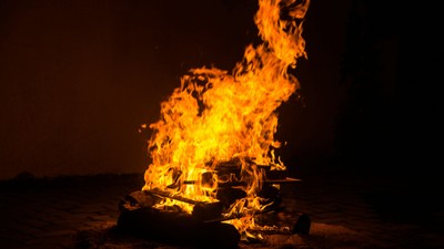 Lebhafte Flammen umhüllen einen brennenden Holzstapel in einer dunklen, nächtlichen Umgebung.