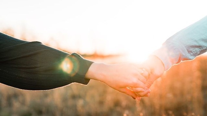 Zwei Personen halten sich an den Händen in einem Feld bei Sonnenuntergang