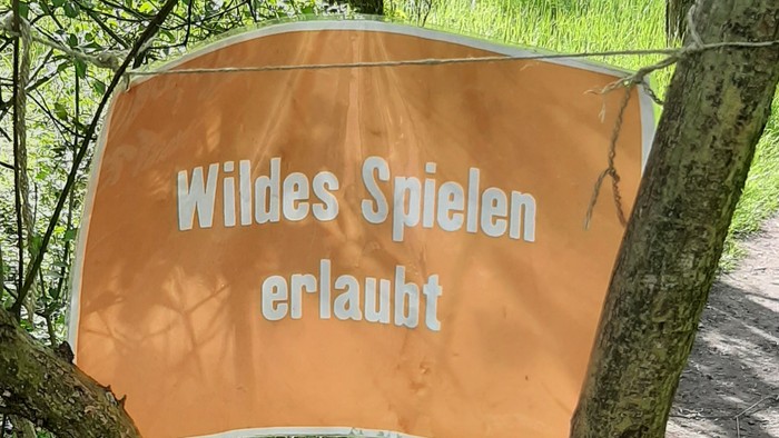 Oranges Banner mit weißer Schrift hängt an Baum im Wald