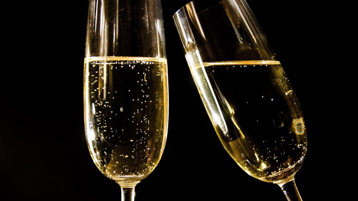 Zwei Champagnergläser mit prickelndem Getränk vor schwarzem Hintergrund