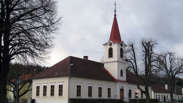 Weißes Kirchengebäude mit rotem Turm und umgebenden Bäumen
