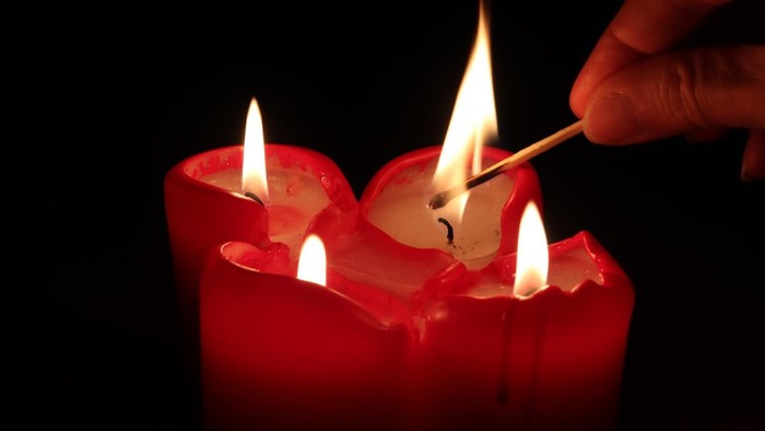 Eine Hand zündet mit einem Streichholz eine rote Kerze an.