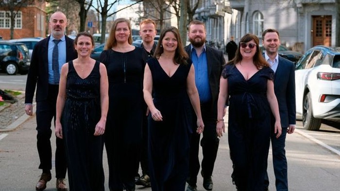 En gruppe af ni personer går i kæde på gaden, alle klædt i formel sort.