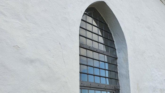 Et smalt buevindue med sort stangværk i en hvid mur.