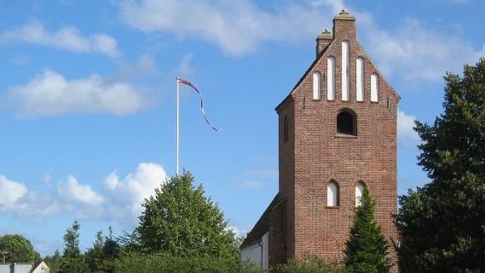 En rød murstenskirke med tårn og hvide vinduer ved en vej.