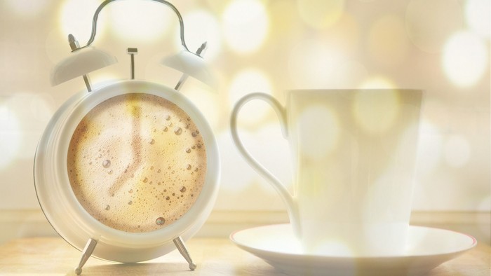 Ein Wecker und eine Tasse Kaffee auf einem Holztisch