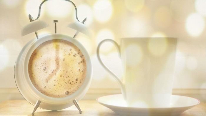 Ein Wecker und eine Tasse Kaffee auf einem Holztisch