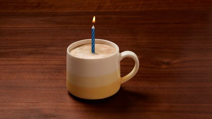 Eine Tasse mit Kaffee und einer Kerze darauf steht auf einem Holztisch.