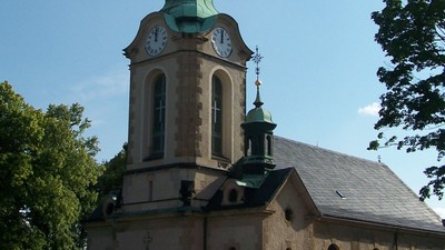 Kirchturm mit Uhr und Kreuzfahne vor blauem Himmel