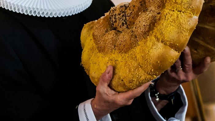 En person holder en stor, rund kage med nødder på.