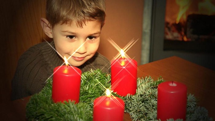Ein Junge sitzt vor einem Adventskranz mit vier brennenden Kerzen.