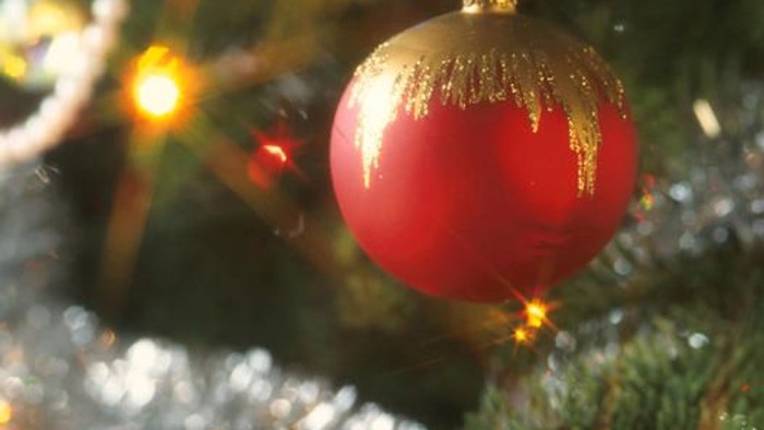 Ein roter Christbaumschmuck mit goldener Spitze hängt an einem Tannenbaum.