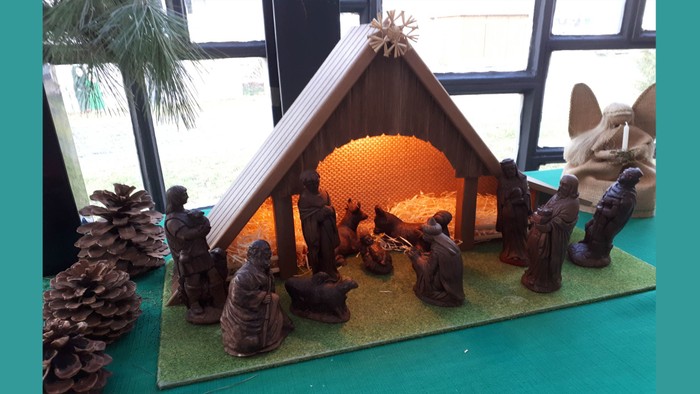 Eine Krippe mit Holzfiguren und Stroh, umgeben von Tannenzapfen und einer kleinen Tanne