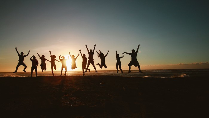 Gruppe springt fröhlich gemeinsam bei Sonnenuntergang am Meeresufer, als Silhouetten vor dem leuchtenden Himmel.
