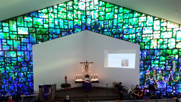 Farbenfrohe Kirchenfenster, Altar mit Kruzifix und Kerzen, Projektionsbildschirm