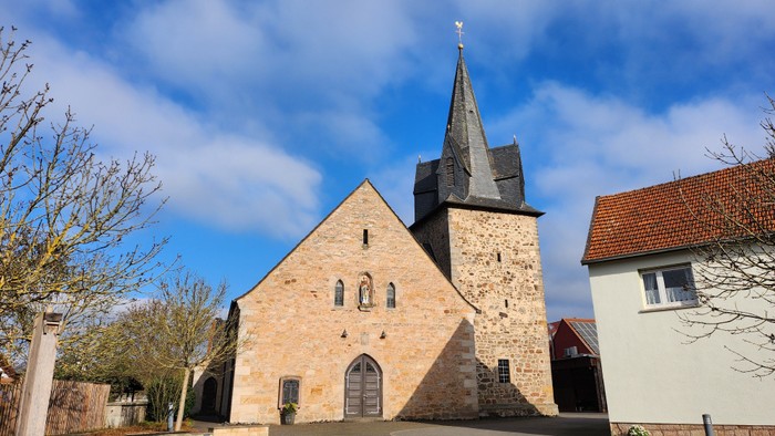 Altsteinige Kirche mit hohem Turm neben weißem Gebäude unter blauem Himmel