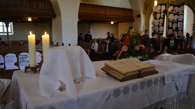 In der Kirche wird eine Messe gefeiert, mit Kerzen, Blumen und Gläubigen.