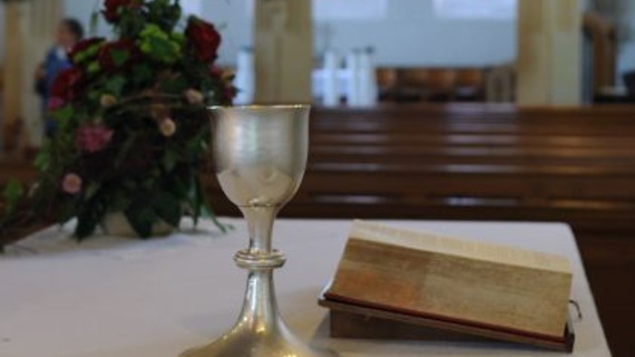 Auf dem Tisch stehen ein Kelch, ein Buch und ein Teller mit Hostien in einer Kirche