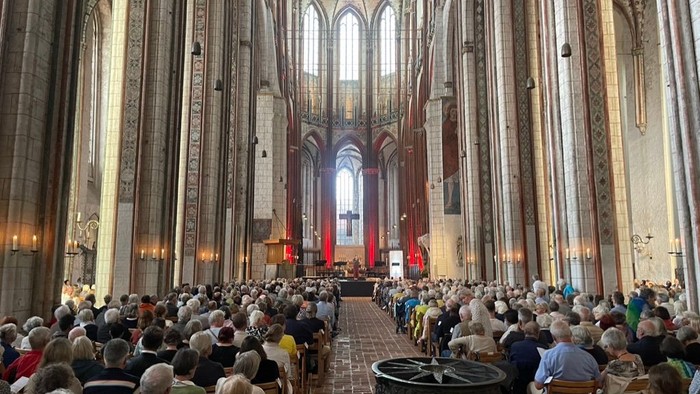 Große Kirche mit vielen Menschen, hohe Decken und bunte Fenster.
