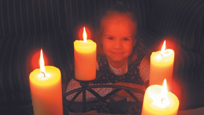 Ein Mädchen sitzt vor vier brennenden Kerzen
