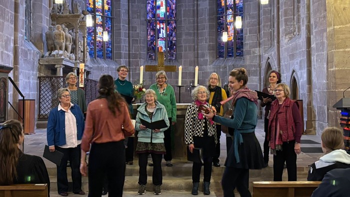 Eine Gruppe von Menschen, die in einer prächtigen Kirche mit bunten Glasfenstern und steinerner Architektur singen.