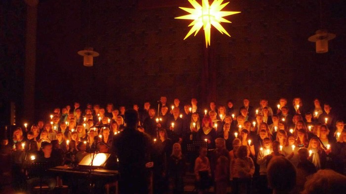 Ein großer Chor singt bei Kerzenlicht, eine helle Sternlampe erleuchtet die Szene.