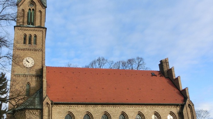 Historische Steinkirche mit rotem Ziegeldach und hohem Uhrturm unter klarem Himmel.