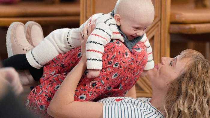 En kvinde holder glædeligt og legende en smilende baby op i en hyggelig indendørs omgivelse.
