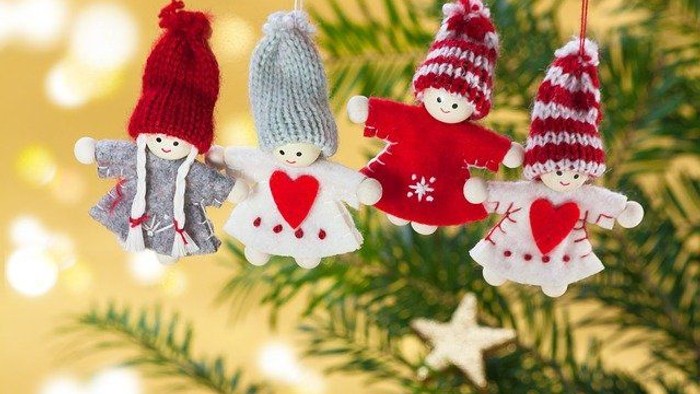 Four festive ornaments hang on a Christmas tree, each depicting a child in winter attire with heart motifs.