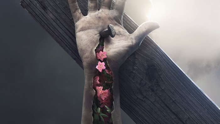 Eine Hand hält ein Holzkreuz mit rosa Blumen, vor einem dramatischen Himmel