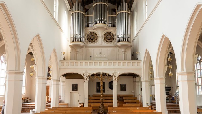 Innenansicht einer Kirche mit Orgel, hölzernen Bänken und hohen Rundbögen.