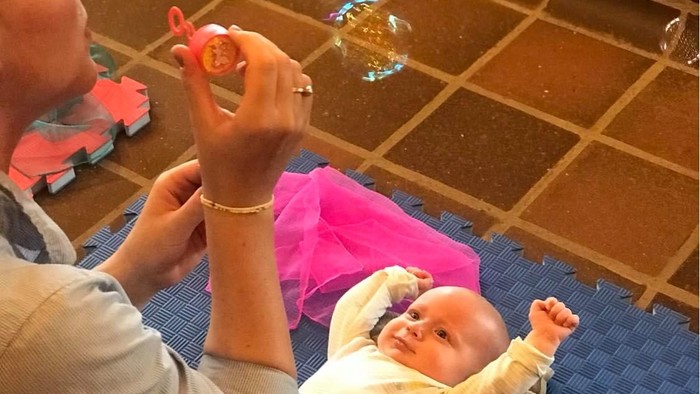 En mand spiller bobleblæser for et barn på en blå matte.