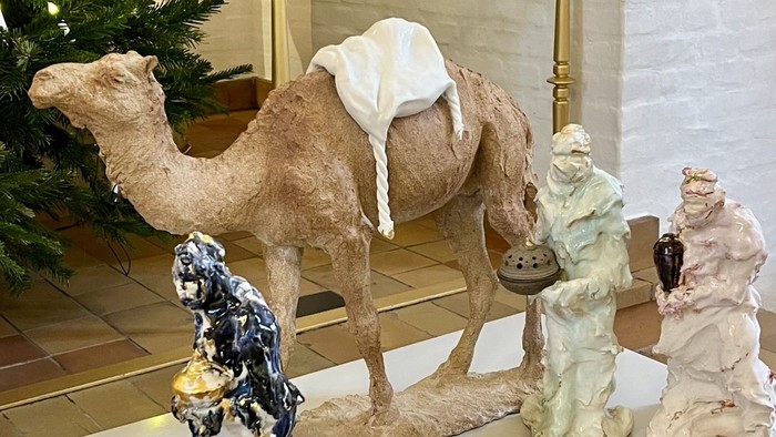 Billedet viser en opstilling af tre keramiske figurer og en kamel på en bord.