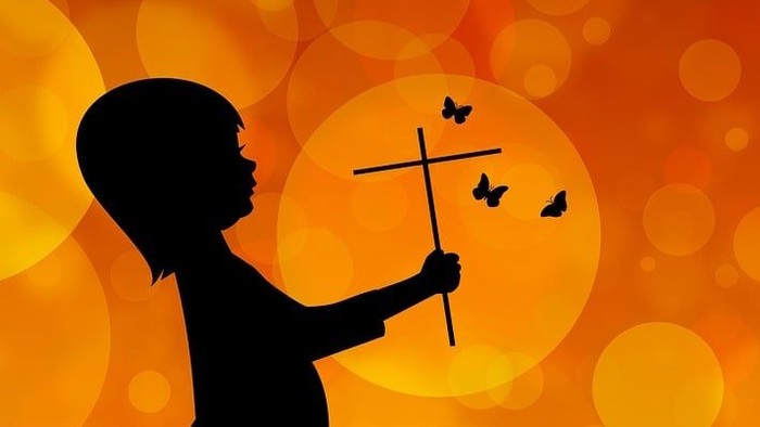 Ein Kind hält ein Kreuz vor einem orangefarbenen Hintergrund mit Schmetterlingen.