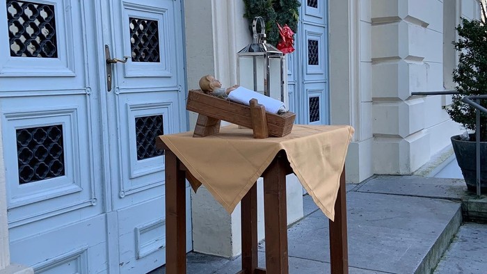 Ein Holztisch mit einer beigen Tischdecke und einer Topfpflanze davor, vor einer weißen Tür.