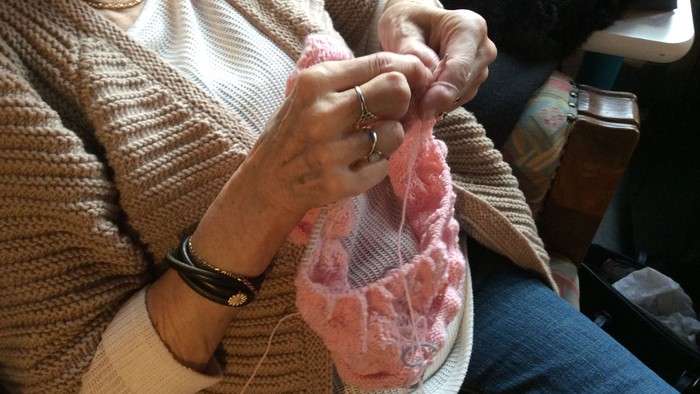 En person sitter og stråler en rosa garne i et stue.