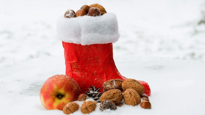 Ein roter Weihnachtsstrumpf gefüllt mit Nüssen und Äpfeln im Schnee